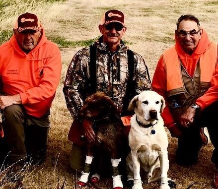 Three men in hunting gear with two hunting dogs