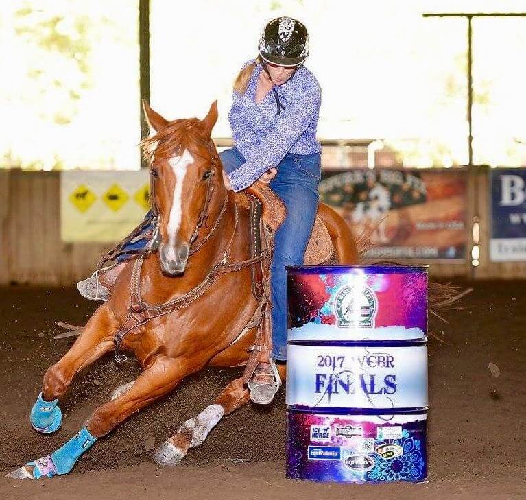 A rider on a galloping brown horse maneuvering around a barrel
