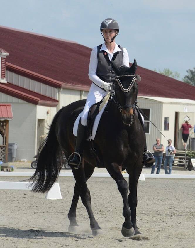 A rider in a white derby outfit riding a black horse