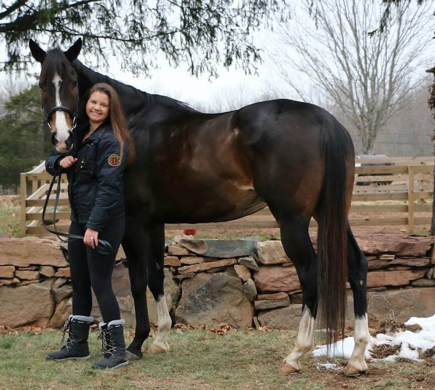 A woman standing next to a dark brown horse