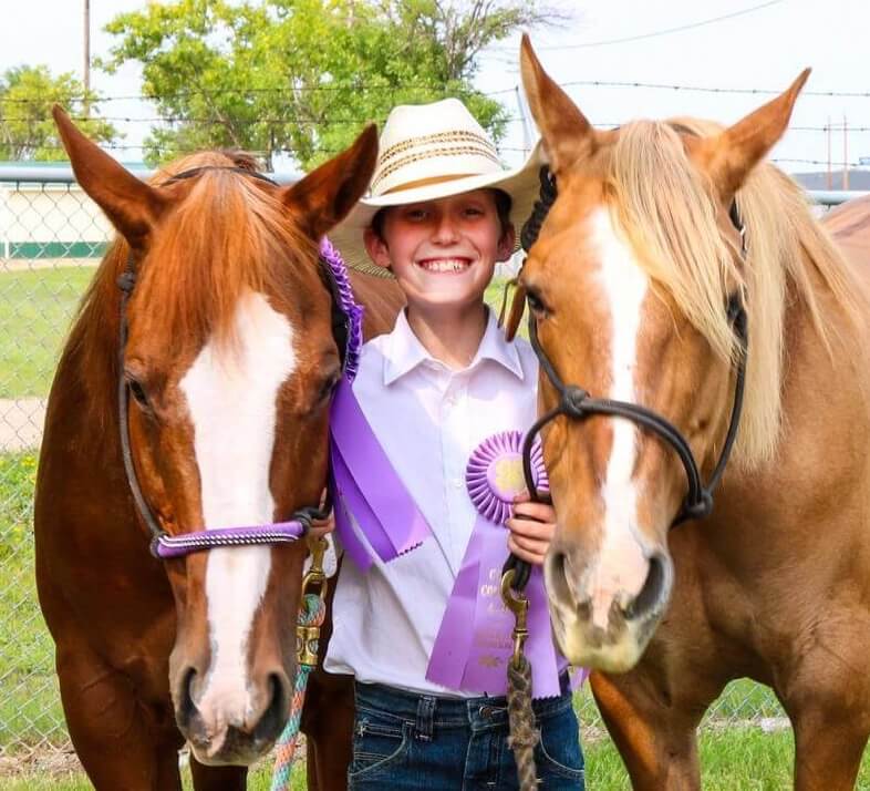 A smiling child in between two horses