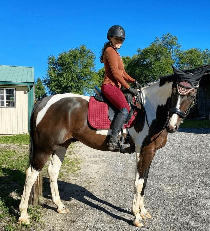 Woman riding a brown and white horse on a gravel driveway